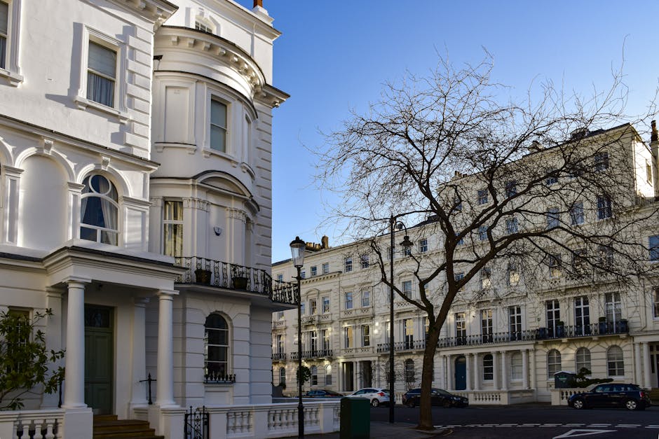 A row of Victorian-style terraced houses in Soho Square with brick facades and decorative bay windows painted in various shades of blue, cream, and green. The buildings feature detailed architectural 